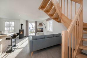 A modern living room with a wooden staircase, a sofa, a dining area, and a fireplace.