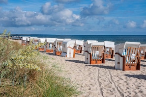 Strandstühle reihen sich an einem Sandstrand mit Blick auf das Meer.