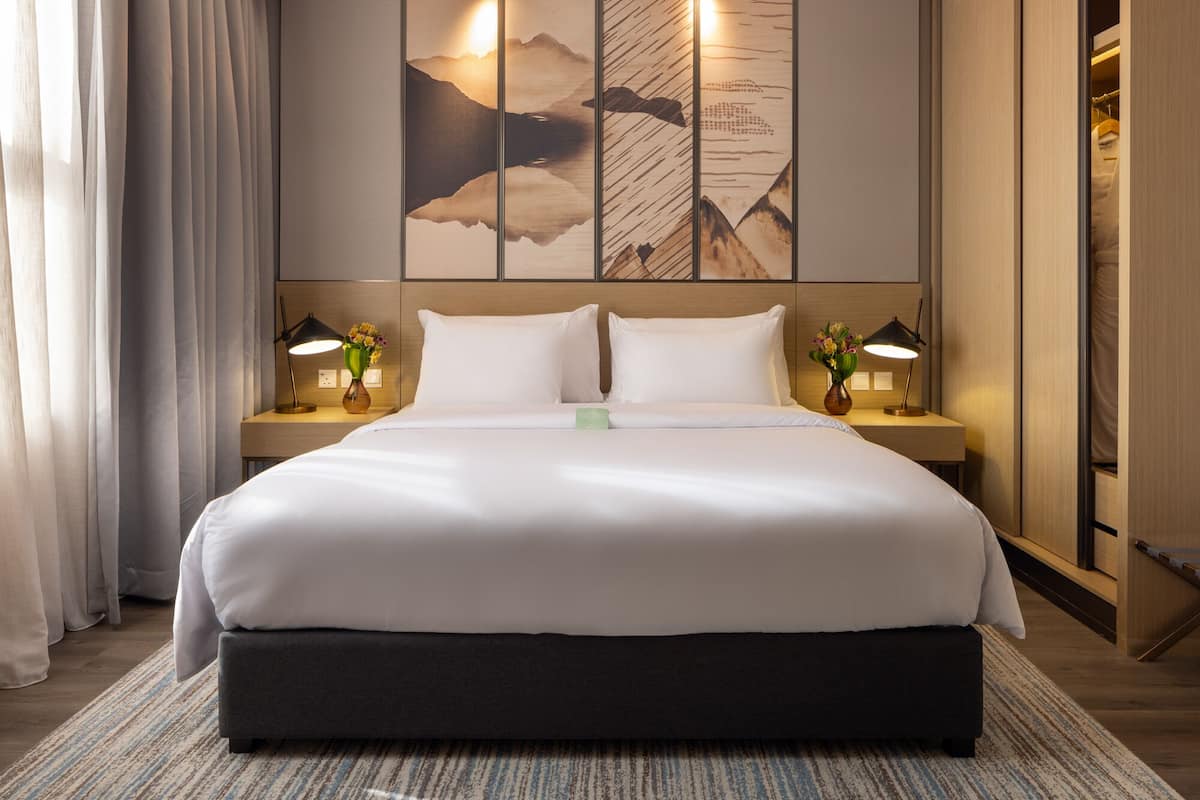 Una cama bien hecha con sábanas blancas, dos mesitas de noche con lámparas y una gran obra de arte en la pared sobre la cama.