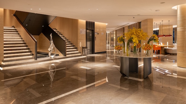 Un vestíbulo moderno con piso de mármol, un mostrador de recepción central y una escalera.