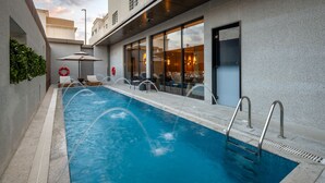 Piscina interior moderna con agua cristalina, rodeada de sillones de descanso y vistas a un restaurante.