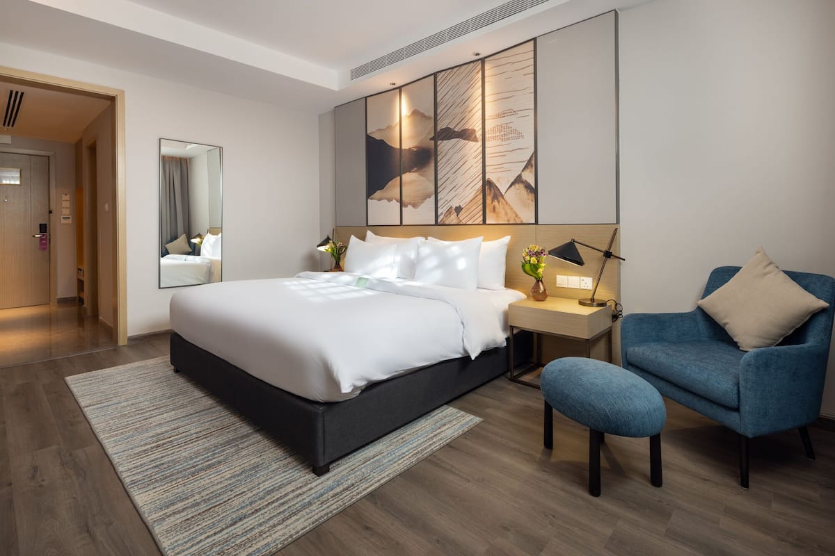 Habitación de hotel moderna con una cama grande, un escritorio, una silla y una obra de arte de gran tamaño en la pared.