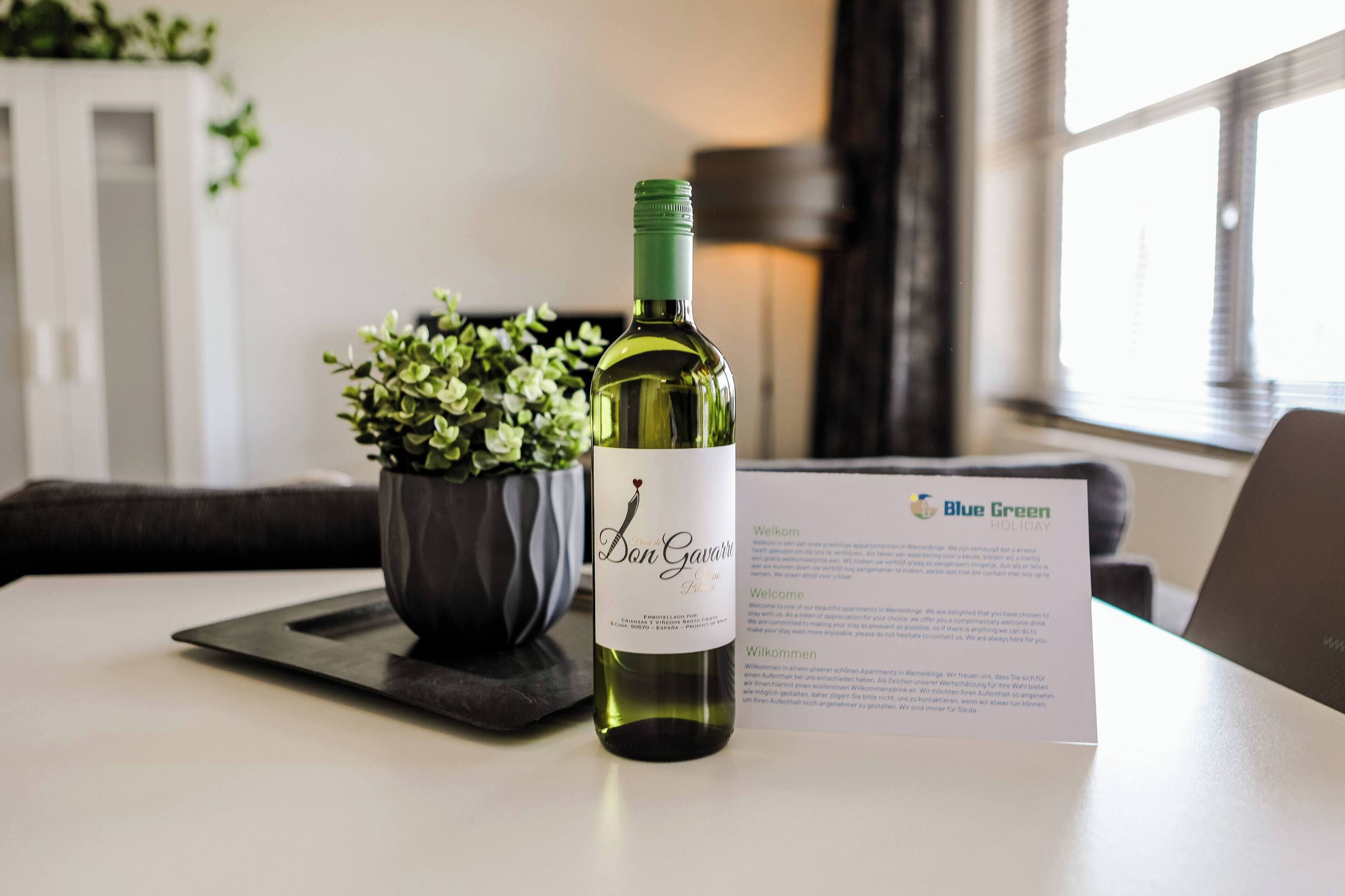 A bottle of wine, a potted plant, and a welcome card on a table.