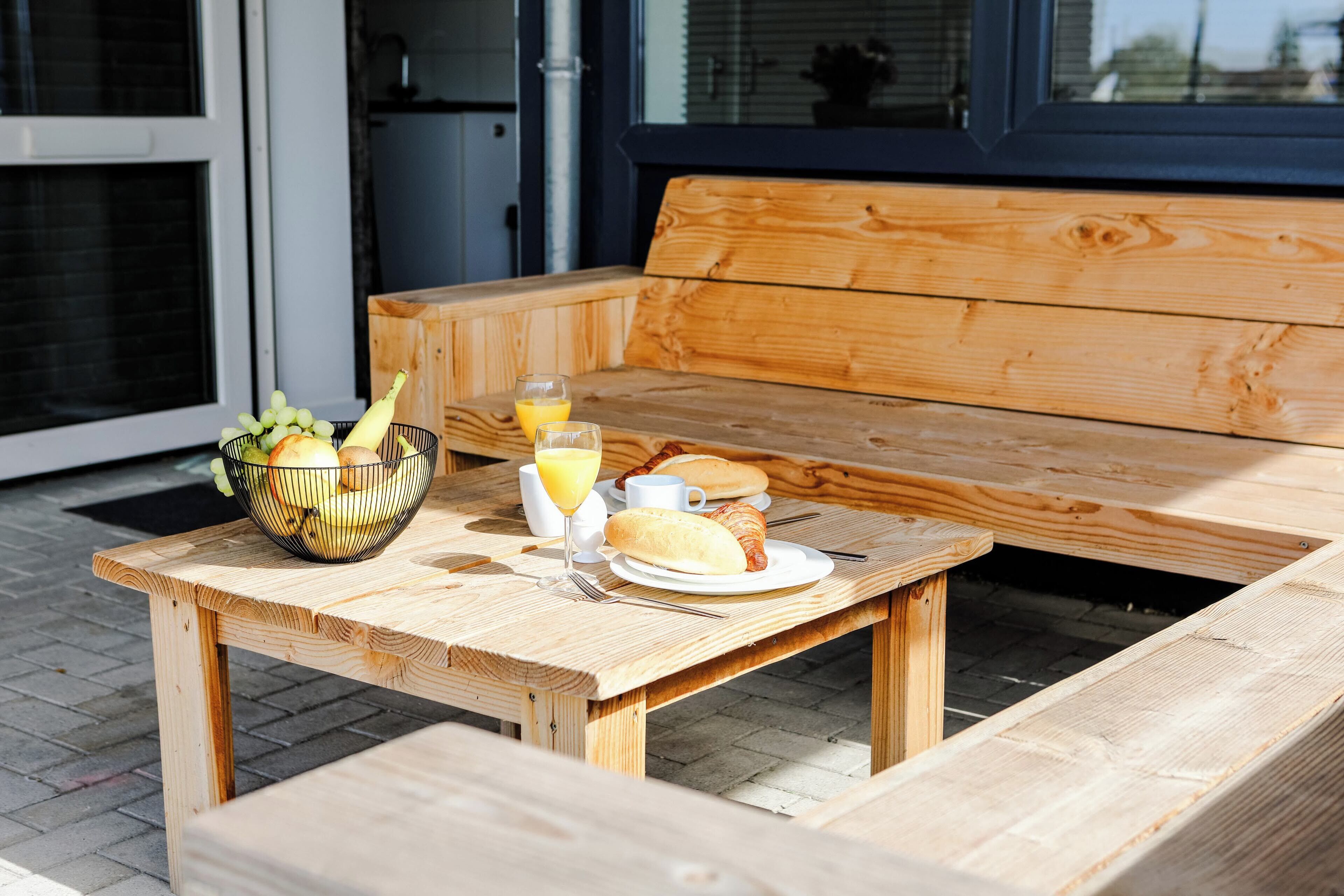 Una mesa de madera con alimentos para el desayuno, incluyendo un croissant, un vaso de jugo de naranja y un bol de fruta.
