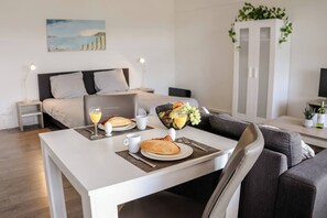 Habitació d'hotel moderna amb un llit ben fet, una taula de menjador preparada per l'esmorzar i vista al mar per la finestra.