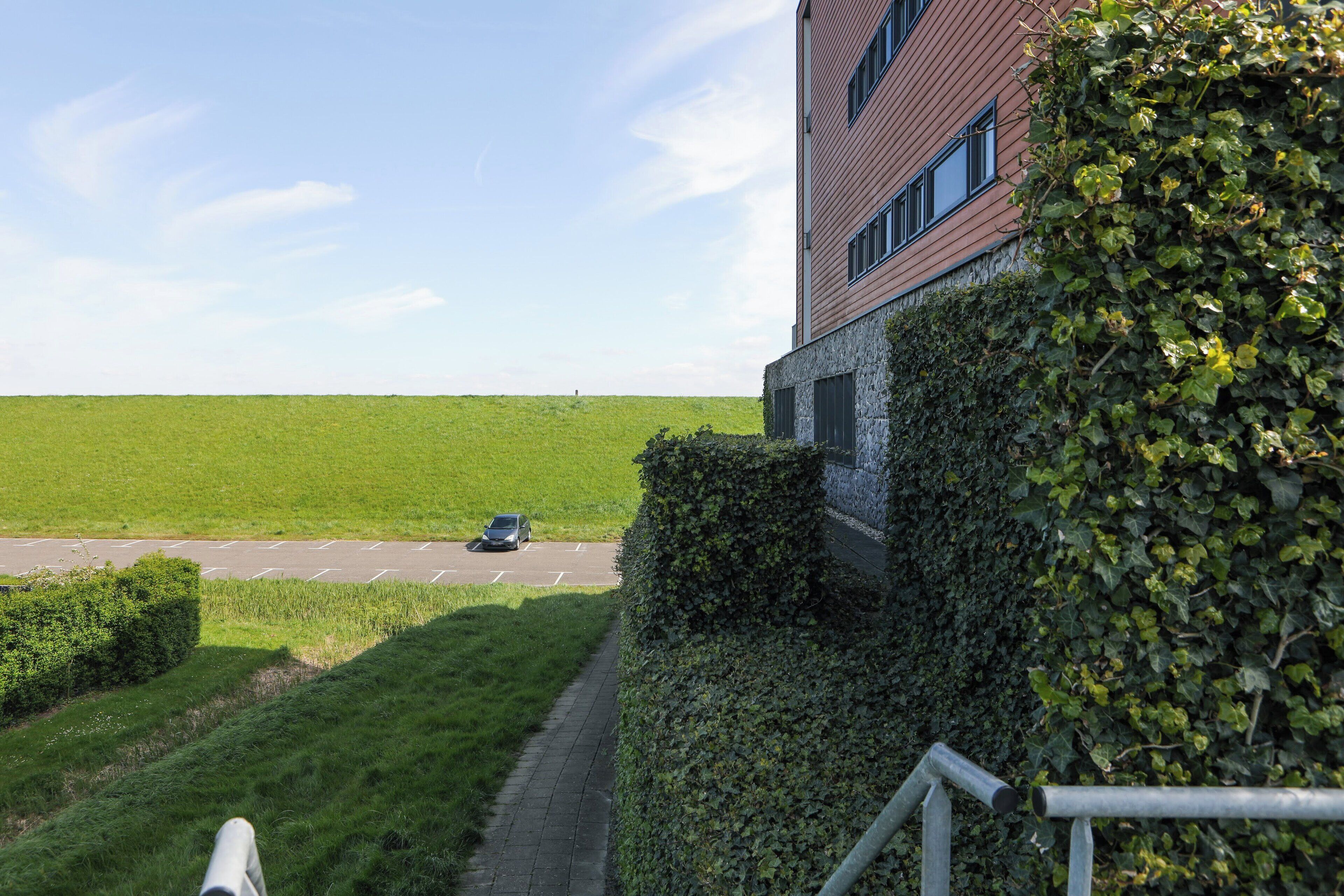 Ein Gebäude mit einer Ziegel-Fassade und einem Heckenbewuchs davor.