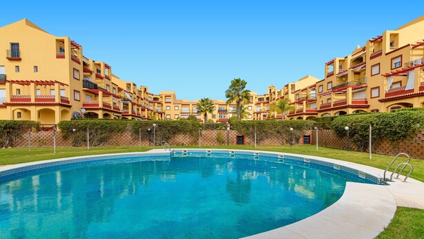 Una piscina rodeada de edificios altos con balcones y un cielo azul despejado.