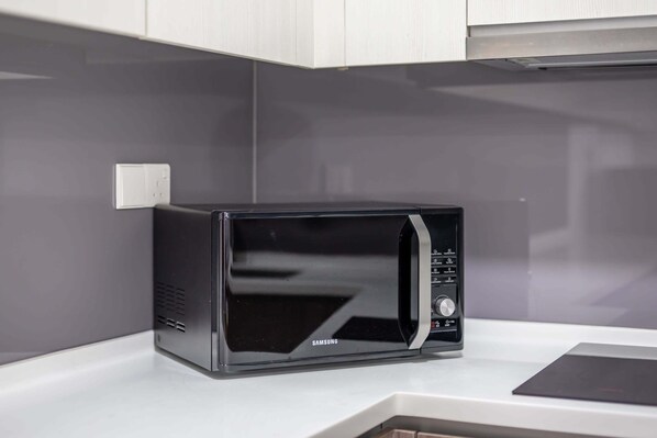 A black Samsung microwave on a white countertop with a gray backsplash and white cabinets.