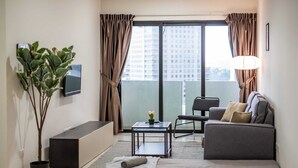 A modern living room with a sofa, a coffee table, a TV, a potted plant, and a balcony with curtains.