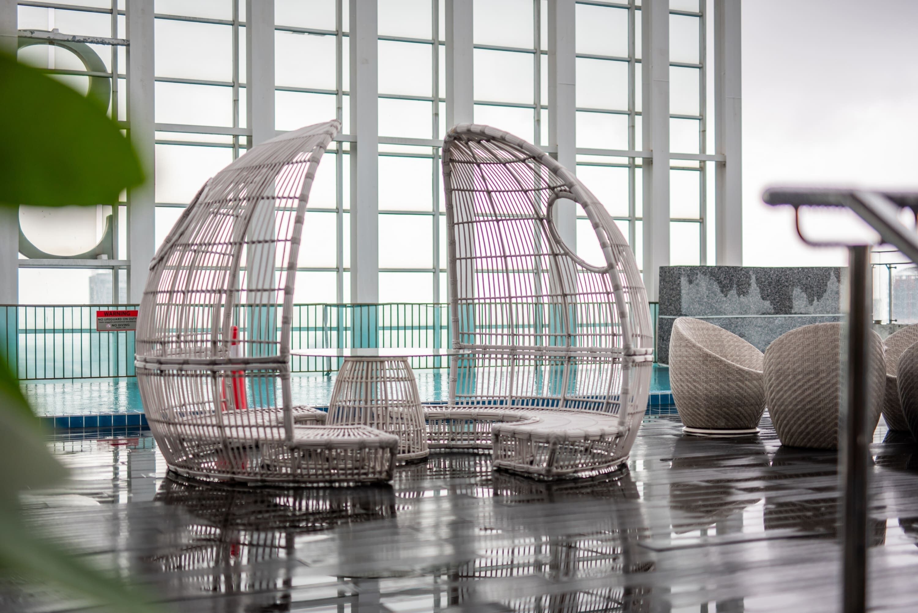 Un espace intérieur moderne doté de grandes fenêtres, de meubles en osier et d’un sol humide.