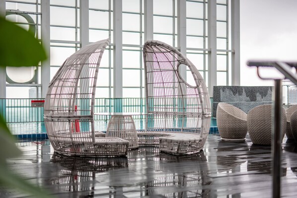 Un espacio interior moderno con ventanas amplias, mobiliario de mimbre y suelo húmedo.