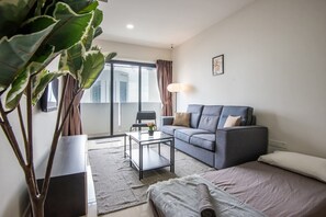 Un salon moderne avec un canapé, une table basse, une plante et une vue sur l’extérieur.