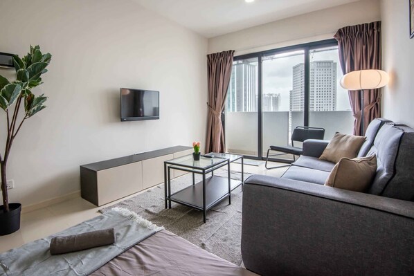Un salon moderne avec un canapé, une table basse en verre, un téléviseur fixé au mur, une grande fenêtre avec des rideaux et une plante en pot.