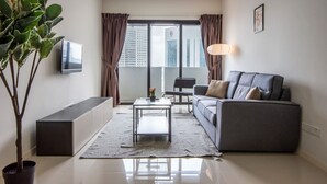A modern living room with a sofa, a coffee table, a TV, a potted plant, and a view of buildings through a large window.