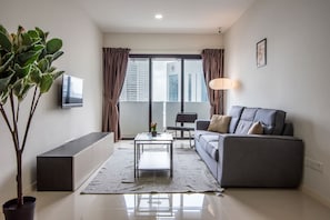 Ein modernes Wohnzimmer mit einer Couch, einem Couchtisch, einem Fernseher, einer Topfpflanze und Blick auf Gebäude durch ein großes Fenster.