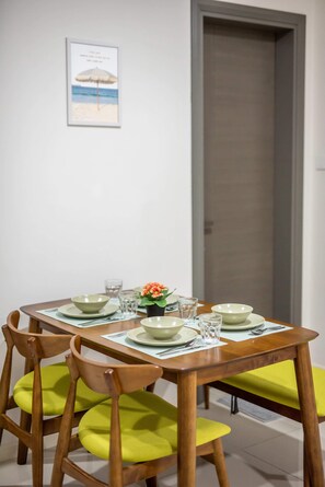 Une table à manger dressée avec des assiettes, des bols et des verres, entourée de chaises en bois dotées de coussins verts.