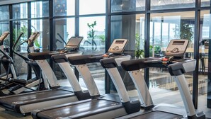 A row of treadmills with digital displays in a modern gym with large windows.