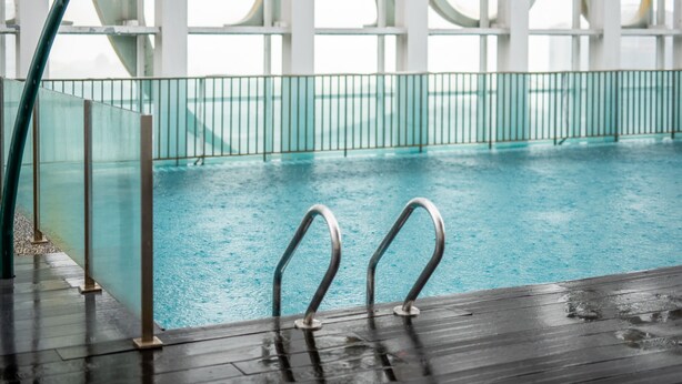 An indoor swimming pool with clear water, metal railings, and a wooden deck.