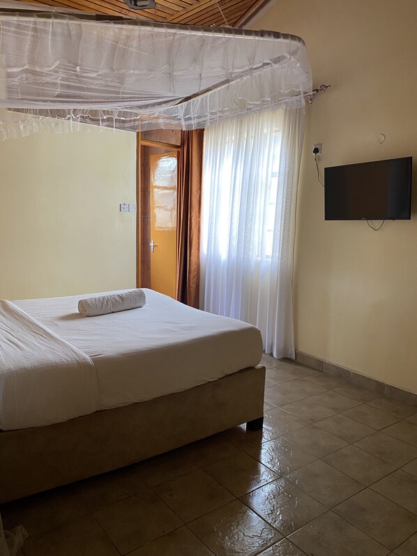 Una habitación de hotel con cama, televisión y ventana con cortinas.