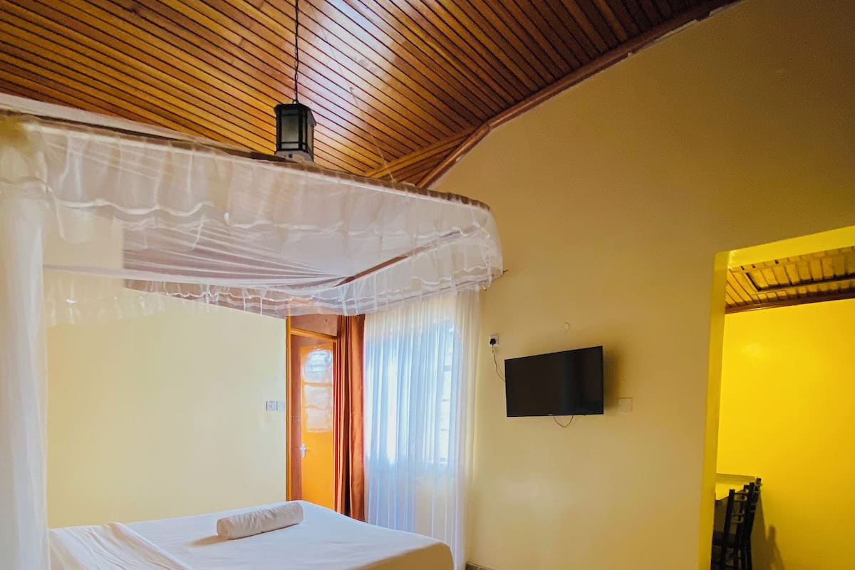 A room with a bed under a canopy, a television on the wall, and a dining area with chairs.