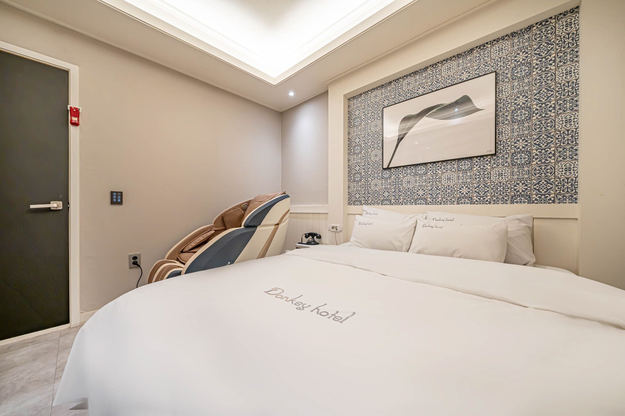 A hotel room with a skylight, a bed with a 'Denker hotel' sign, patterned wallpaper, and a framed picture on the wall.