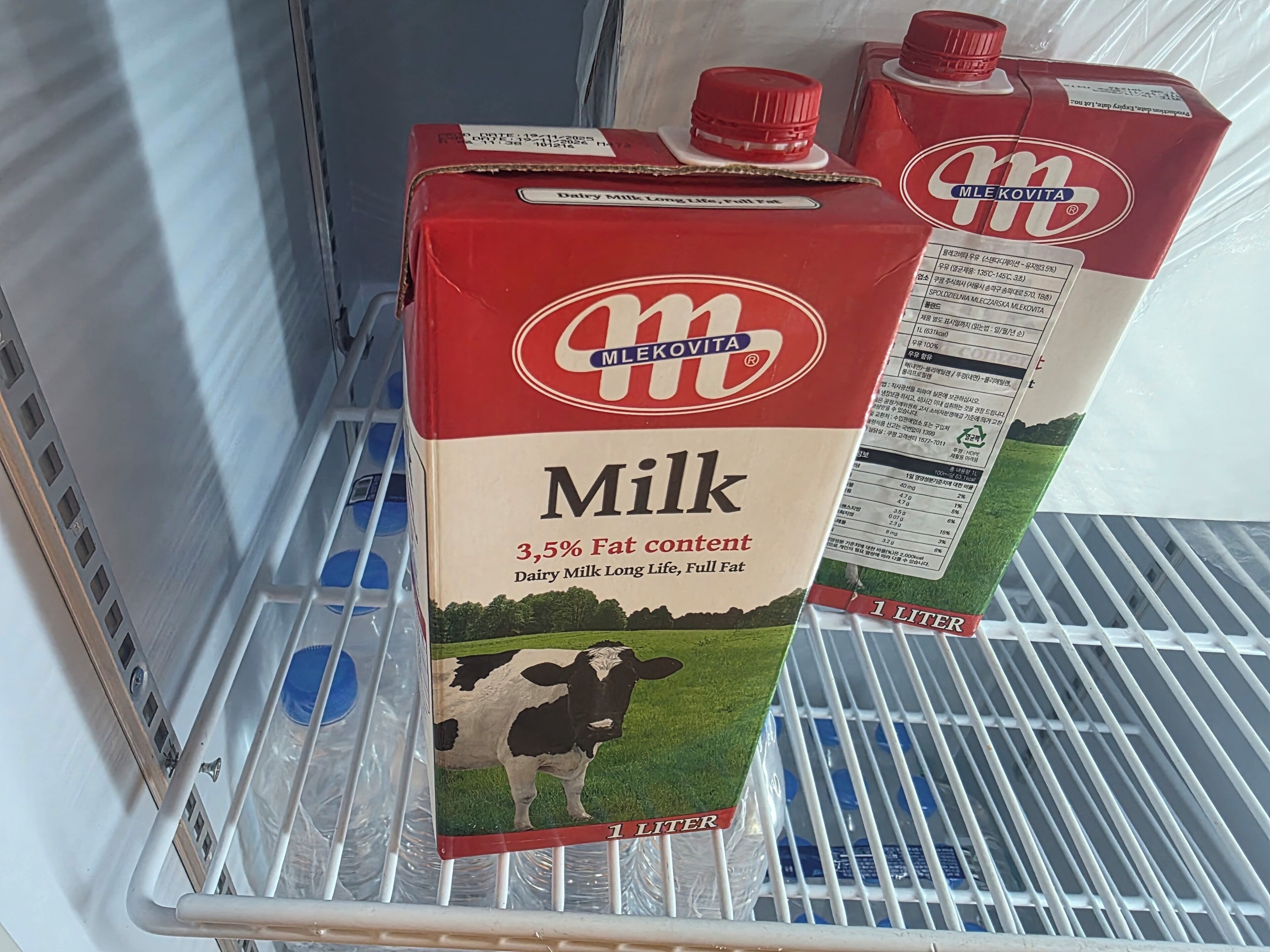 Una repisa de refrigerador con dos cartones de leche.