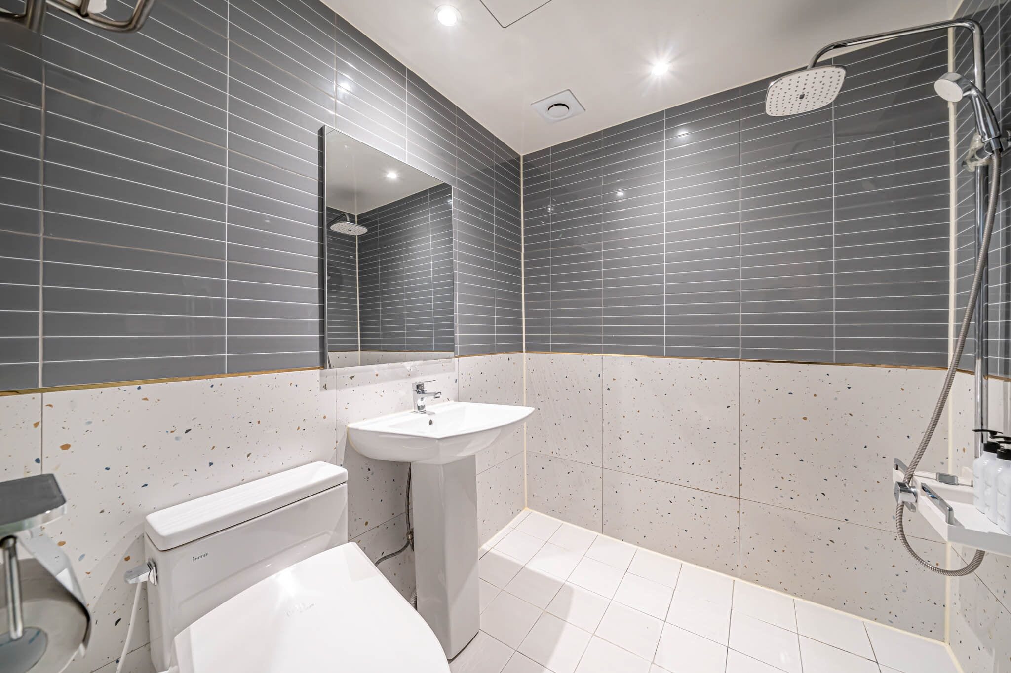 A modern bathroom with grey tiled walls, a white sink, a toilet, and a shower.