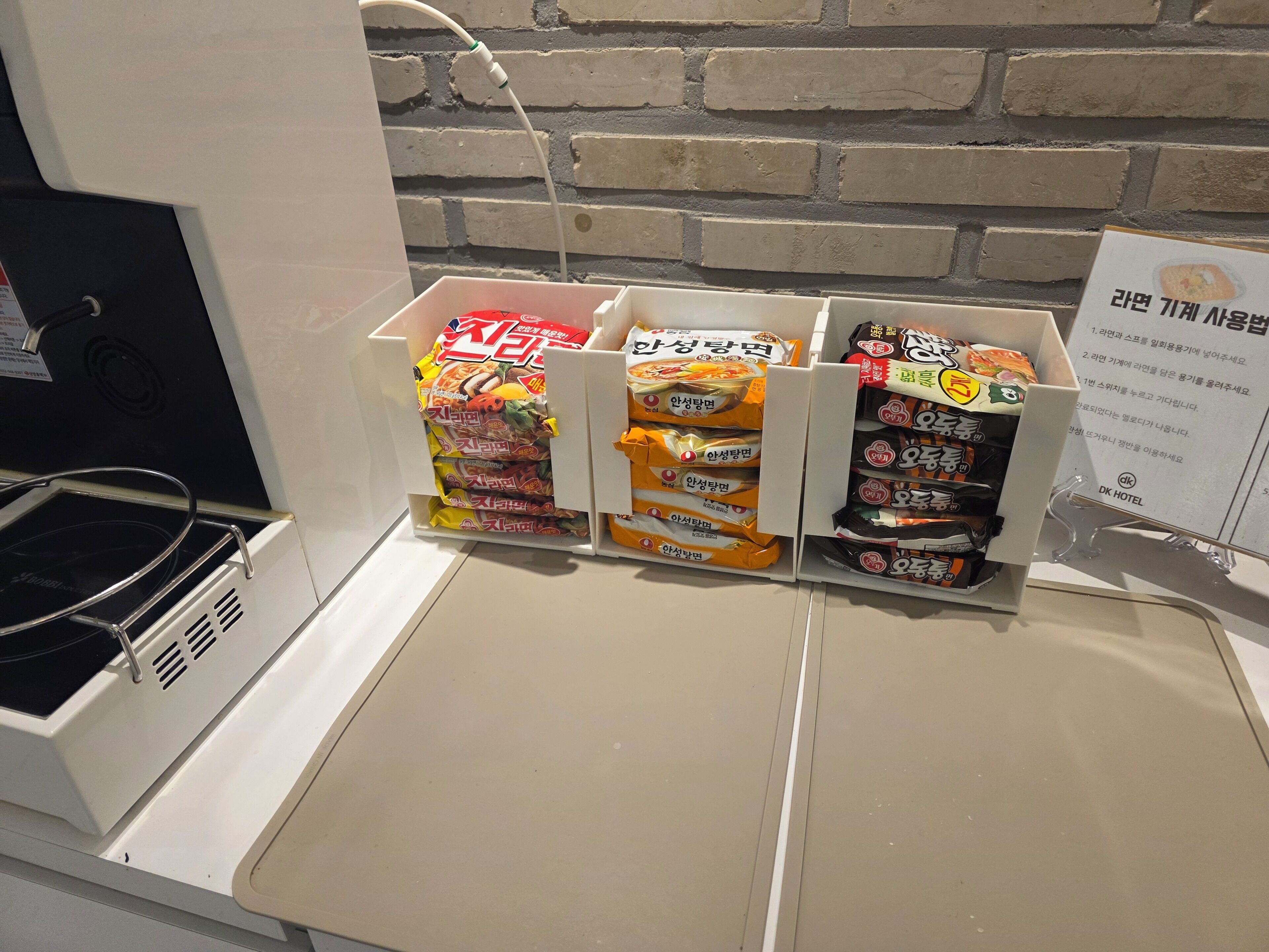 A hotel room with a kitchenette area featuring a stove and a sink. There are snack packages neatly organized on a shelf.