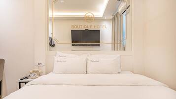 Habitación de hotel con cama, teléfono en la mesita de noche, televisor de pantalla plana sobre la cama y un espejo que refleja la habitación.