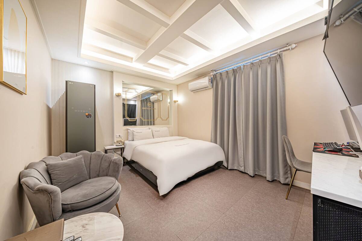 A hotel room with a bed, a desk, a chair, a couch, and a mirror.