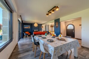 Un coin repas avec une table dressée pour quatre personnes, des chaises, un lustre et une vue à travers une porte vitrée.