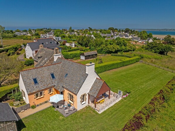 Une grande maison dotée d’une terrasse, d’une pelouse et offrant une vue sur la mer.
