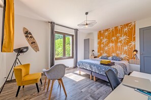 Une chambre moderne avec un lit, un bureau et une chaise, de grandes fenêtres et un mur décoré sur le thème des tropiques.
