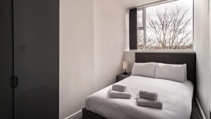 Un dormitorio moderno con un ventanal grande, una cama bien hecha y una mesita de noche con lámpara.