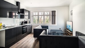 Una cocina moderna con armarios oscuros, un ventanal grande y una zona de estar con sofá y mesa de centro.