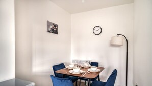 Comedor con una mesa de madera dispuesta para cuatro, sillas azules, un reloj en la pared y una lámpara de pie.