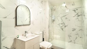 Un baño con pared de azulejos de mármol, un lavamanos, un inodoro y una ducha con cerramiento de vidrio.