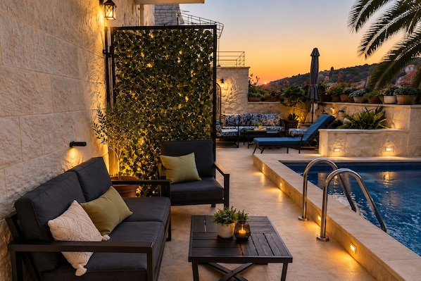 A poolside area with a sofa, chairs, a table, and a decorative wall with plants.