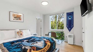 A modern bedroom with a large bed, a desk, and a window with a view of trees. - The Boy Who Lived, Harry Potter's Sweet Suite (Seattle)
