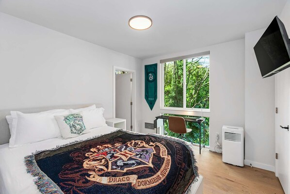 Un dormitorio con cama, escritorio, silla, televisor y ventana con vistas a zonas verdes.