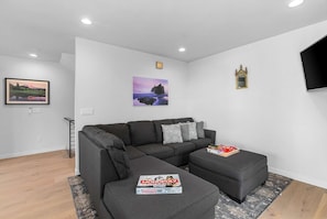 Ein modernes Wohnzimmer mit einem grauen Sofa, einem kleinen Hocker und einem gerahmten Bild an der Wand.