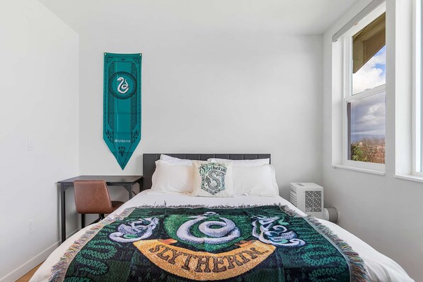 A bedroom with a bed, a desk, and a window.