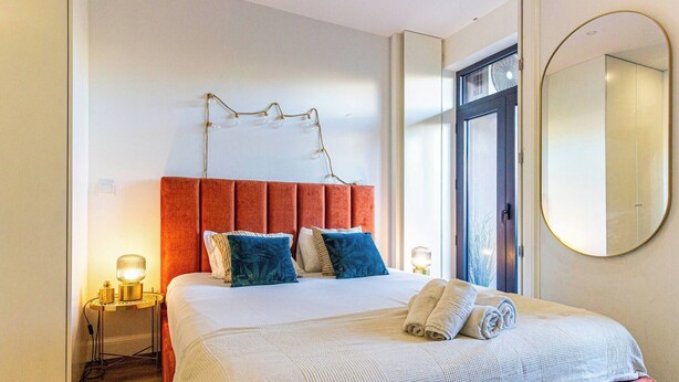Ett hotellrum med en stor säng, en röd sänggavel och en rund spegel på väggen.