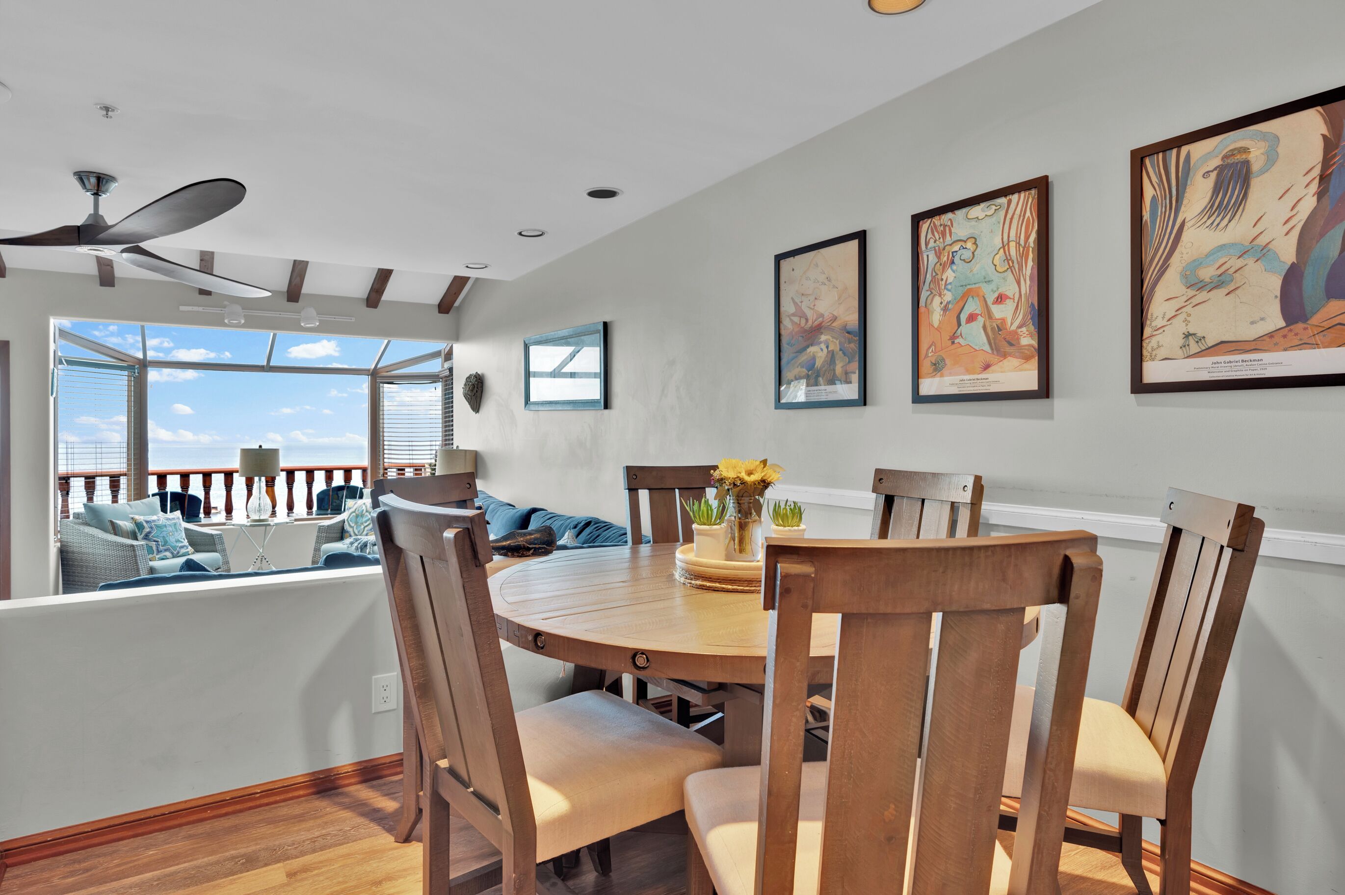 Un coin repas avec une table ronde, des chaises en bois et une vue sur l’océan grâce à de grandes fenêtres.
