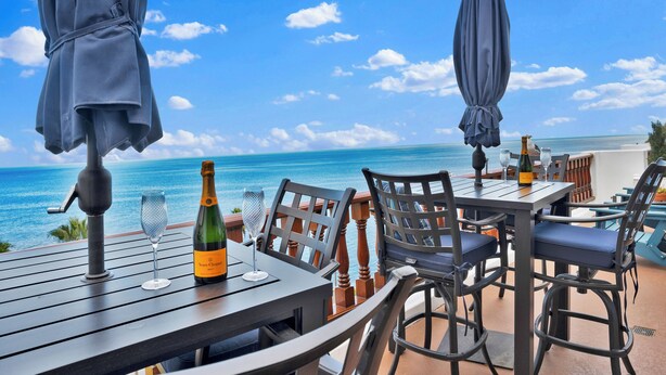 Ein Essbereich im Freien mit Tisch, Stühlen und Sonnenschirmen mit Blick auf das Meer.