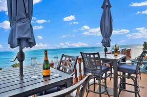 An outdoor dining area with a table, chairs, and umbrellas overlooking the ocean.