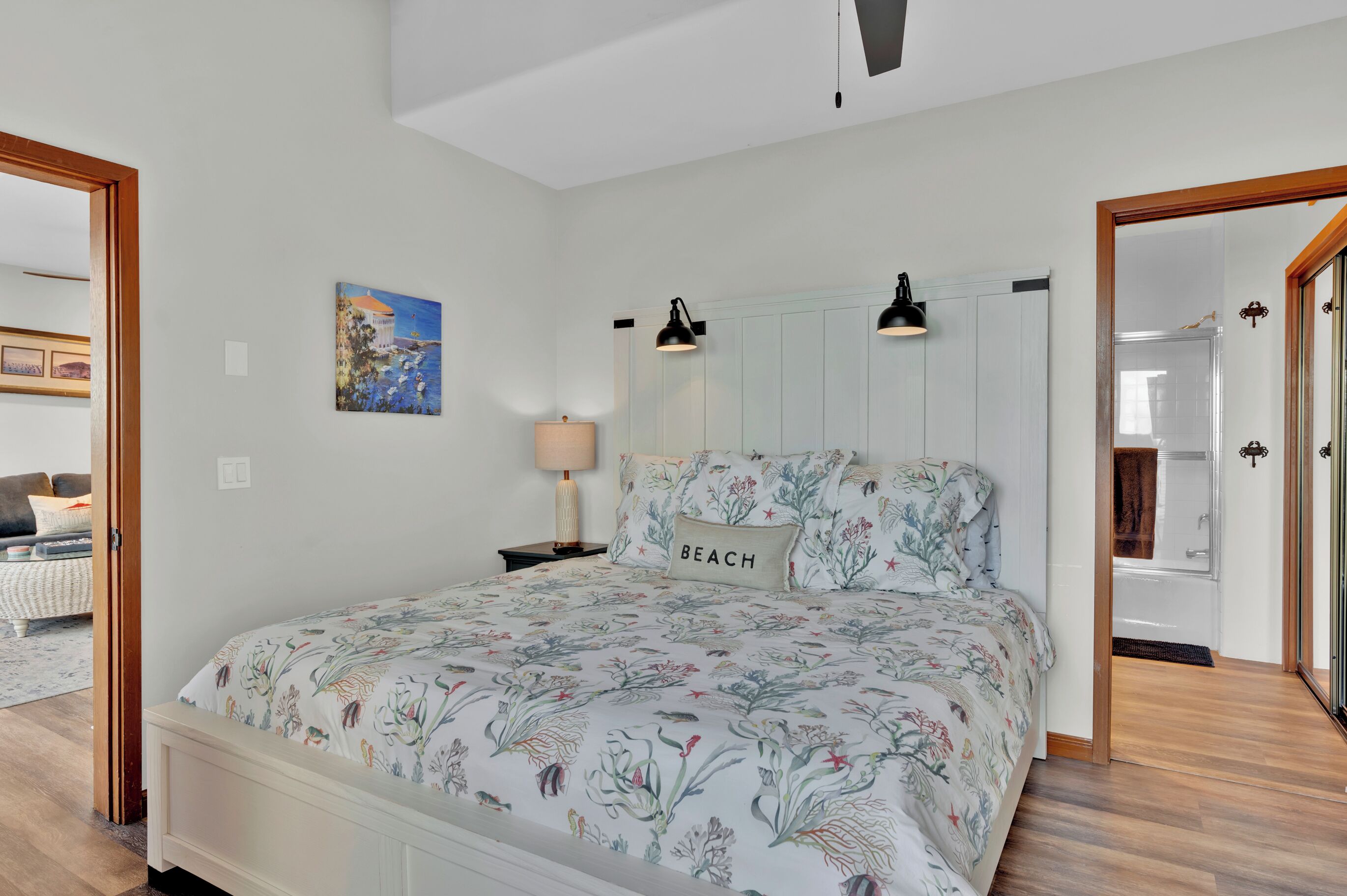 A bedroom with a floral bedspread, a bedside lamp, a painting on the wall, and a door leading to another room.