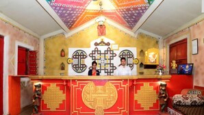 A room with a red and gold altar, two statues, and a bed with patterned bedding. - Chokhi Dhani Indore (Indore)