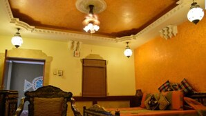 A room with a wooden ceiling, a bed with colorful bedding, a wooden chair, and a decorative wall hanging. - Chokhi Dhani Indore (Indore)