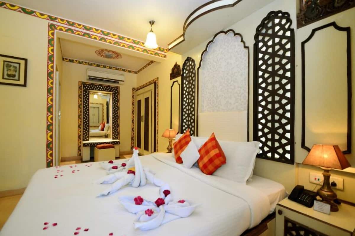 Habitación de hotel con una cama bien hecha, una lámpara de noche, un teléfono y un espejo decorativo.